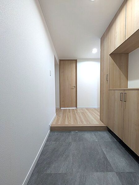 温かみのある木目調の収納と、落ち着いたトーンの玄関床が調和した空間。明るい照明が心地よいエントランスを演出します。