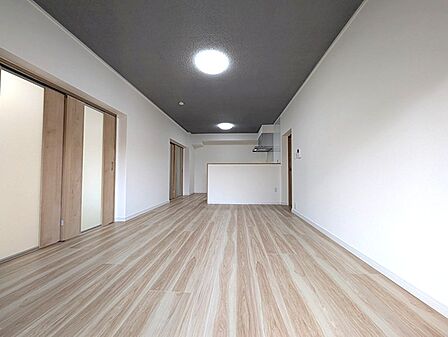 木目のフローリングと白い壁、ダークグレーの天井が調和する、モダンなリビングダイニング。隣接する居室を開放すれば、さらに広々とした空間に。
