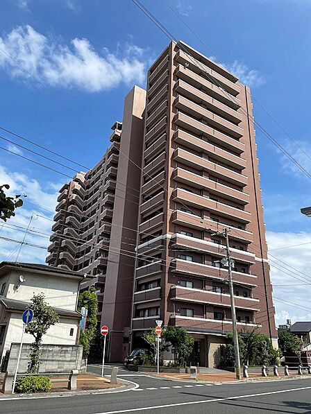 堂々とした佇まいのマンション。青空の下、落ち着いた色合いの外観が目を惹きます。暮らしやすさを予感させる住環境です。