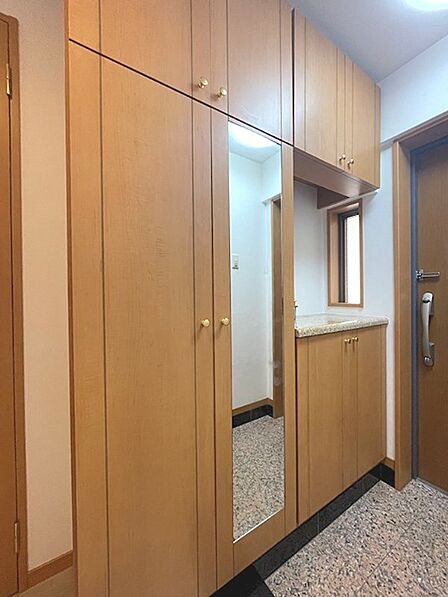 明るい木目調の玄関収納は、姿見付きで出発前の身だしなみチェックにも便利です。天井までの高さがあり、たっぷりと収納できます。