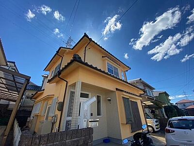外観：青空が広がる明るい日差しが差し込む邸宅。周辺には戸建て住宅が立ち並び、穏やかな住環境が魅力です。