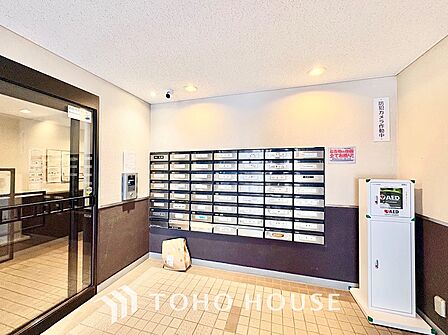 居住者のプライバシーを守る奥まった設計の郵便受けスペース。ステンレス製のダイヤル錠付きポストが整然と配置され、明るい照明と広い通路で日々心地よく手紙や書類を確認できます。