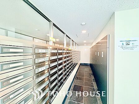 居住者のプライバシーを守る奥まった設計の郵便受けスペース。ステンレス製のダイヤル錠付きポストが整然と配置され、明るい照明と広い通路で日々心地よく手紙や書類を確認できます。