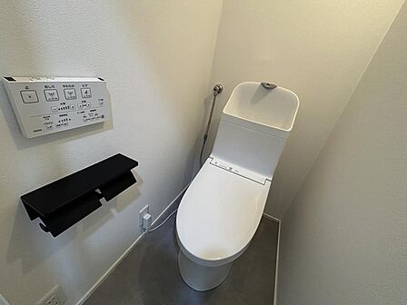 新規交換された、清潔感あふれる温水洗浄便座付きトイレ。壁掛けタイプのリモコンや、小物が置けるスタイリッシュなペーパーホルダーを備えています。