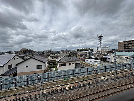 4階バルコニーからの眺めです。目の前を鉄道の線路が通り、その先には戸建てを中心とした街並みが広がります。前に高い建物がなく、空が広く見えます。※AIによる家具消し加工を行なっております。