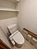 トイレ：操作部を備えたトイレです。便器と上部の棚、壁面のペーパーホルダーをご覧いただけます。ご家族で使う水回りの設備や配置を、ほかの写真とあわせてお確かめください。※AIによる家具消し加工を行なっております。
