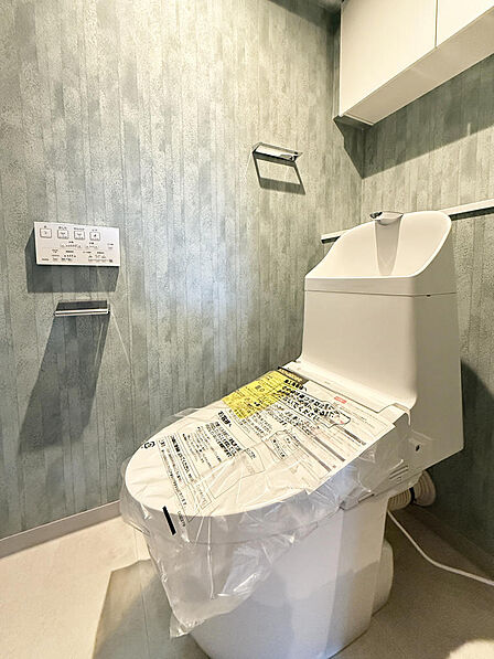 シックなアクセントクロスが目を惹く温水洗浄便座付きトイレ。上部にはトイレットペーパーなどを隠せる棚を備えています。