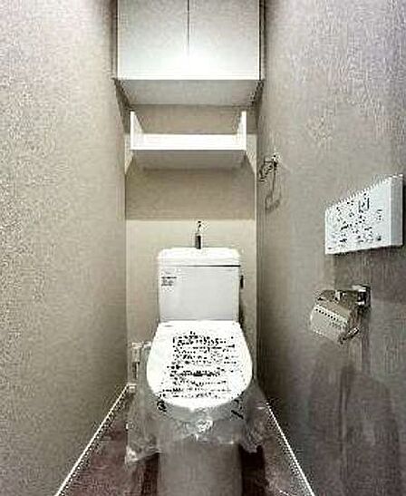 ウォシュレット機能付きのトイレ。ペーパーホルダーやタオル掛けは標準装備しています。また、上部には吊戸棚があるので、トイレットペーパーのストックや清掃道具等を収納するのに便利です。