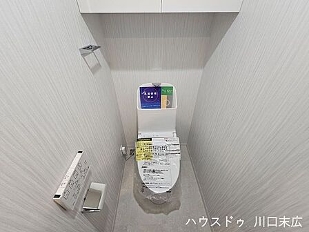 温水洗浄便座と上部吊戸棚を備えたトイレ空間。トイレットペーパーや清掃用品をスッキリと収納できます。