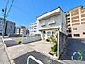 その他：《建物外観》白を基調とした外壁に出窓や窓飾りがアクセントとなった個性的なデザインが印象的な住まい。道路側からは建物の形状や敷地の広がりを確認でき、玄関周りの植栽が温かみのある雰囲気を演出しています。