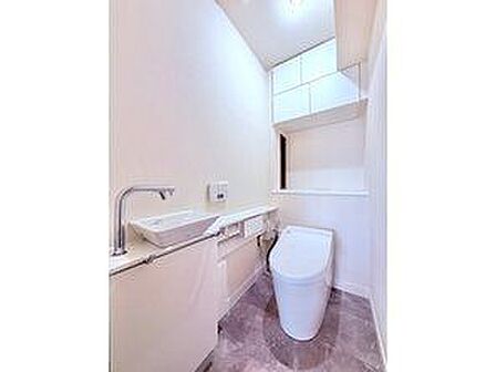 ウォシュレットのついた温水洗浄便座のトイレです。扉付きの吊戸棚もあり、掃除用具や予備のトイレットペーパーなども隠してたっぷり収納できます。手洗い機は壁面にあり、お子様も洗いやすいです。