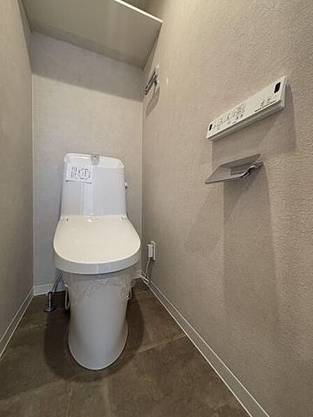 ウォシュレットのついた温水洗浄便座のトイレです。暖房便座、脱臭、乾燥機能などを搭載し、トイレットペーパーの使用量を減らして清潔を保ちます。棚もあり掃除用具や予備のトイレットペーパーなども収納できます。