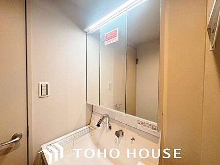 大型の鏡(または三面鏡仕様)を備えた、機能的なシステム洗面化粧台。身支度がしやすい広い洗面ボウルや、散らかりがちな洗面小物をスッキリと隠して片付けられる充実の収納スペースが完備されています。