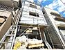 外観：建築中の建物を見上げて撮影した1枚です（2026年10月）。3階建ての高さと、道路側に付く2階と3階の窓の位置が分かります。外壁が仕上がると完成予想図の姿に近づきます。
