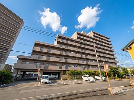 青空に映える落ち着いた色合いの外観。敷地内には駐車場や植栽も整えられています。