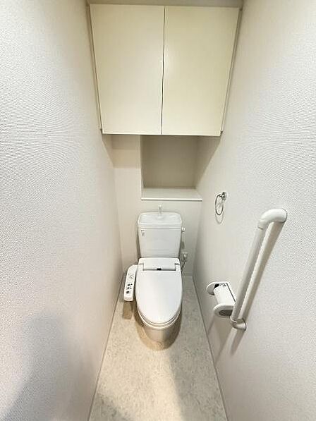 収納スペースが備わっておりトイレまわりの小物もすっきり片付けられます。手すり付きで使いやすさに配慮されています。清潔感のある内装が印象的です。トイレットペーパーの収納もしやすい設計です。