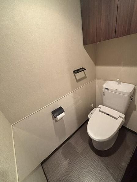 温かみのある壁色とシックな床材が調和したトイレです。機能的な収納スペースが備え付けられておりスッキリとした印象です。便利なウォシュレット機能付きで快適性にも配慮されています。