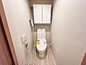 トイレ：収納棚が設置されておりトイレ用品の整理に便利です。壁付けリモコンで使いやすさも考えられています。明るい色合いの床と壁が空間を広く見せています。シンプルなデザインが特徴的です。