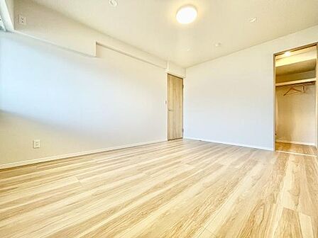 明るい色合いのフローリングが特徴の寝室です。広々とした空間で使い勝手が良さそうです。収納スペースへのアクセスもしやすいです。照明設備も設置されており快適に過ごせる印象です。