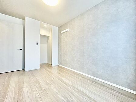 明るい色味のフローリングとグレー調のアクセントクロスが特徴の洋室です。天井照明が部屋全体を照らし開放感のある空間となっています。収納スペースも確保されており整理整頓がしやすいです。