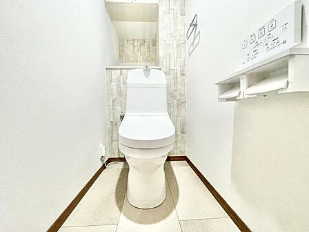 壁や床が明るく清潔感のあるトイレです。収納スペースが設けられており使い勝手にも配慮されています。ペーパーホルダーや操作パネルも設置されています。シンプルな内装でお手入れもしやすい仕様です。