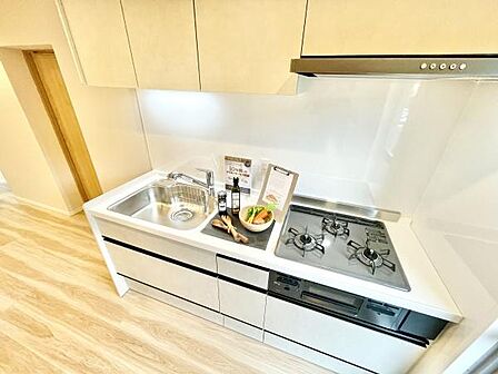 明るい色合いのキッチンが空間をすっきりと見せています。三口コンロと広めのシンクがあり使い勝手が良いです。収納スペースも豊富に確保されています。清潔感のあるデザインが印象的です。