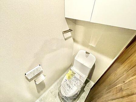 清潔感のあるトイレです。収納スペースが上部に設けられており小物の整理に便利です。ペーパーホルダーと手洗い一体型のデザインが特徴的です。明るい色調で空間が広く感じられます。