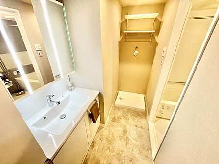 明るい照明が設置された洗面台は広々としたカウンターで使い勝手が良好です。収納スペースが充実しており洗面所全体が整理しやすくなっています。洗濯機置き場も確保されていて家事動線に配慮されています。