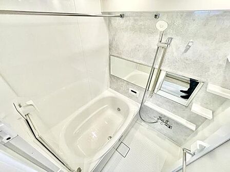白を基調とした明るいバスルームです。広めの鏡が設置されているため空間に開放感があります。手すりや棚もあり利便性が考えられています。浴槽は清潔感がありシャワーヘッドも高さ調節が可能です。