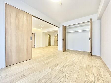 明るい色合いのフローリングと大きなクローゼットが特徴の寝室です。壁や扉も淡い色で統一されており部屋全体がすっきりとした印象です。開放的な空間が広がり清潔感を感じられます。