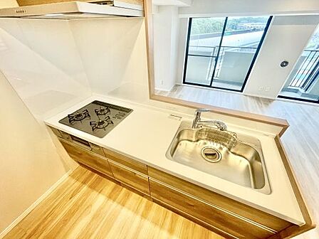 キッチンは明るい色合いのフローリングと調和した空間です。シンクやガスコンロは清潔感があります。作業スペースも確保されています。リビングとの仕切りが低く開放的な印象です。