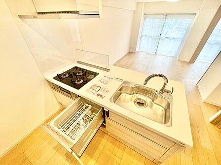 明るい空間にシンプルなデザインのキッチンが設置されています。3口コンロや食洗機が備わっていて機能性が魅力です。シンクや天板も広めに設計されていて使い勝手の良さが伝わります。