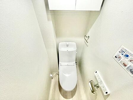 清潔感のあるシンプルなトイレ空間です。収納スペースもあり機能的に使いやすい設計となっています。壁リモコンが設置されているため操作性も良好です。ペーパーホルダーやタオル掛けも完備されています。