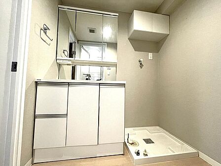 白を基調とした清潔感あふれる洗面スペース。三面鏡付きの機能的な洗面化粧台に加え、洗濯機置場の上部には吊戸棚を備えており、洗剤や日用品をすっきりと収納できる使い勝手の良い空間です。