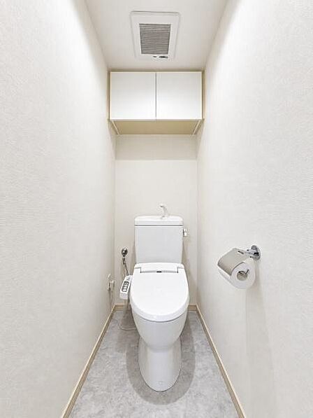 清潔感のあるトイレ空間。上部には収納棚を備え、トイレットペーパーや掃除用品などをすっきり収納できます。温水洗浄便座も設置されており、限られた空間を有効活用した、毎日使いやすい機能的な設備です。