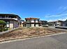 外観：空き地と周囲の住宅が見える住宅街の風景です