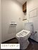 トイレ：清潔感のあるシンプルな内装が魅力のトイレです。壁付け棚が備わっており収納スペースも確保されています。ペーパーホルダーは使いやすい位置に設置されています。換気にも配慮された設計です。