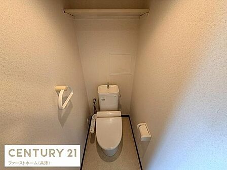 壁際に収納棚が設置されていて使いやすいトイレ空間です。シンプルなデザインで清潔感があります。紙巻き器やタオル掛けも付いていて便利です。空間の有効活用がされています。