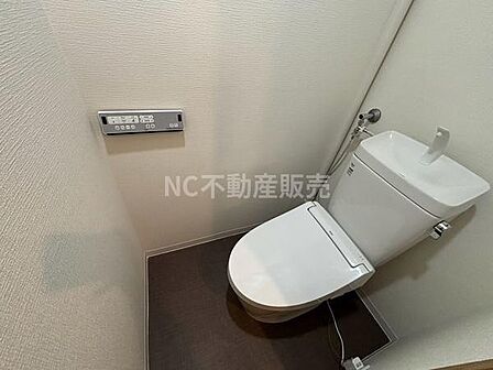 シンプルなデザインのトイレで清潔感のある空間です。壁面に操作パネルが設置されており使いやすさが考慮されています。手洗い付きのタンクが実用的です。床の色合いが落ち着いた印象を与えます。